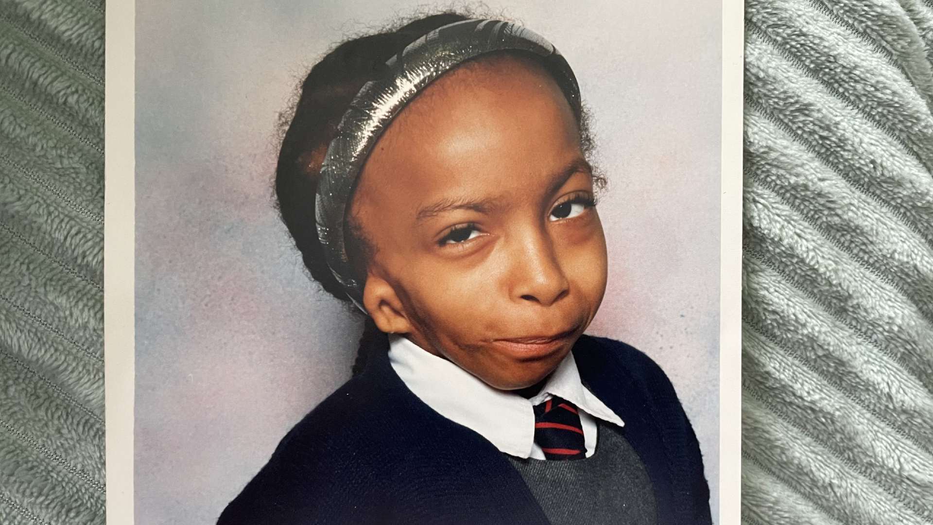 Katy at school. She wears her school uniform and a silver hairband on her head with her hair pulled back.