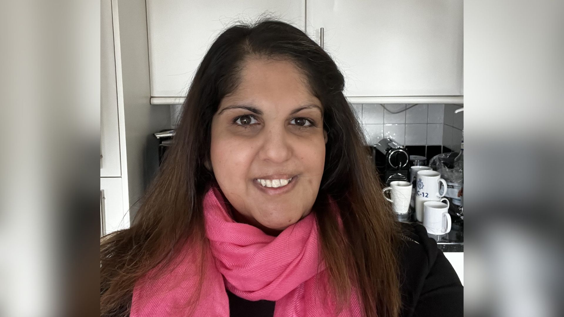 Rekha is wearing a big pink scarf and smiling at the camera.