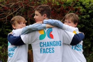 An image of three boys, wearing changing faces t shirts, with arms around each other's shoulders looking back at the camera and smiling